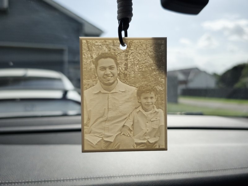 3D-printed car lithophane of a dad and son hanging from a rearview mirror, glowing in the daylight