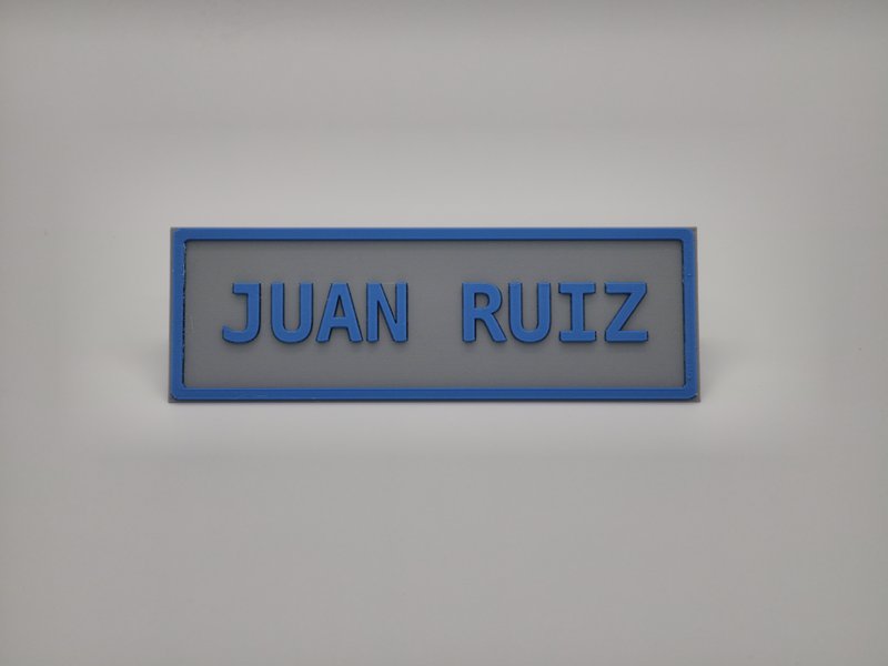 3D-printed two-tone desk name plate reading JUAN RUIZ in Sapphire Blue on Matte Fossil Grey