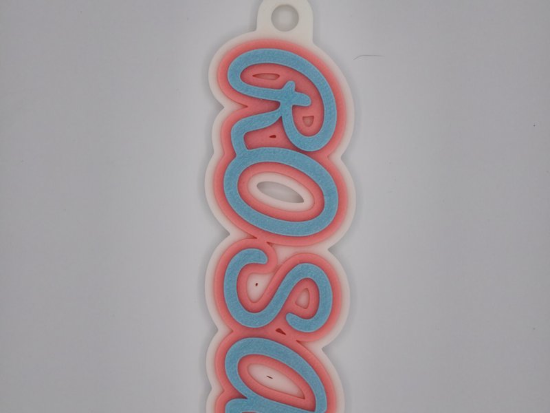 3D-printed ROSA name keychain in cursive script, sky-blue letters with a coral outline on a white base