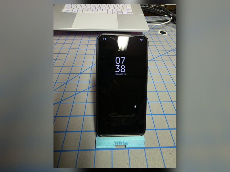 A phone held upright by a blue printed stand on the shop's cutting mat